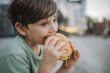 Thoughtful boy eating burger at street - ANAF01996