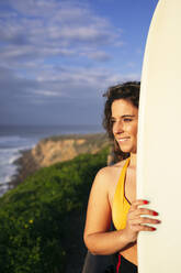 Lächelnde Frau mit Surfbrett an einem sonnigen Tag am Strand - DCRF01751