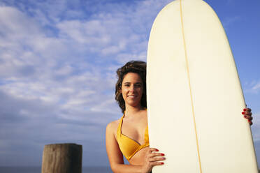 Junge Frau hält Surfbrett an einem sonnigen Tag - DCRF01752