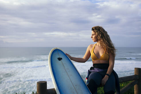 Young woman with surfboard contemplating near sea - DCRF01754