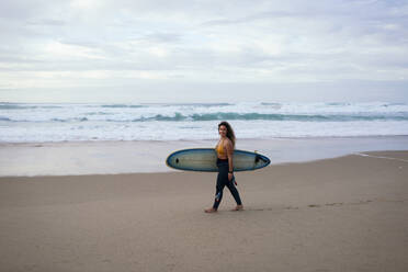 Junge Frau mit Surfbrett am Strand im Urlaub - DCRF01757