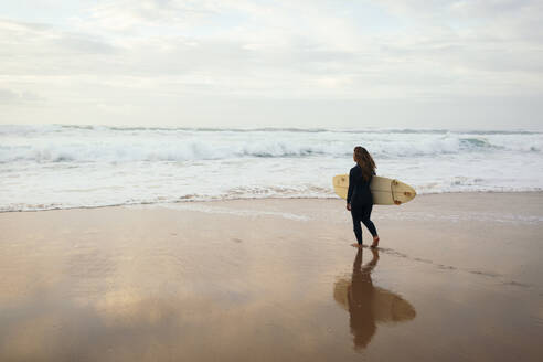 Woman with surfboard walking towards sea at beach - DCRF01760