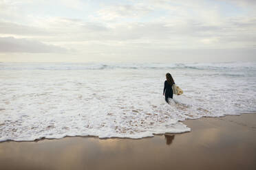 Junger Surfer mit Surfbrett in welligem Meer am Strand - DCRF01761