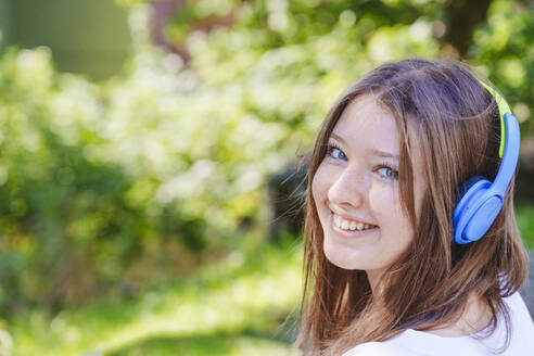 Smiling teenage girl listening music through wireless headphones - IHF01588