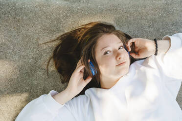 Teenager-Mädchen hört Musik über drahtlose Kopfhörer auf der Straße liegend - IHF01590
