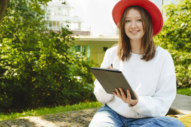 Lächelndes jugendliches Mädchen mit Tablet-PC im Park sitzend - IHF01593
