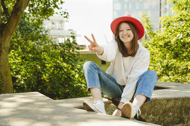 Smiling teenager gesturing peace sign sitting on bench - IHF01595