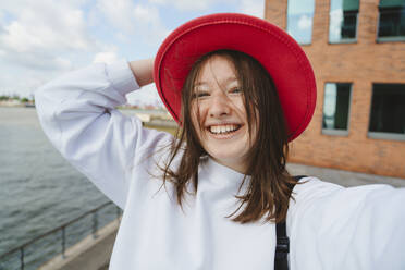Happy teenager with red hat by Elbe river at harbor - IHF01597