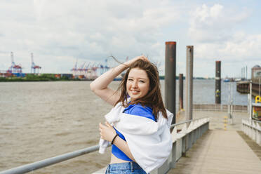 Teenager with hand in hair standing at harbor by Elbe river - IHF01601