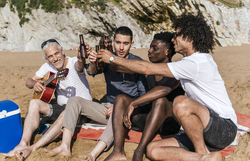 Multi-ethnische Freunde stoßen im Urlaub am Strand mit Bierflaschen an - PBTF00133