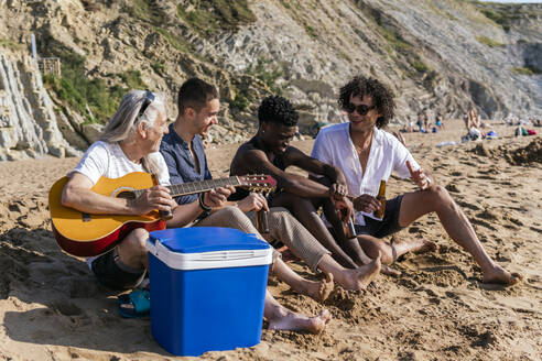 Älterer Mann hält Gitarre und trinkt Bier mit Freunden am Strand - PBTF00138