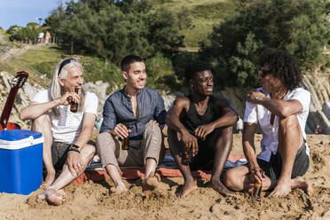 Lächelnde multiethnische Freunde beim gemeinsamen Bier am Strand im Urlaub - PBTF00140