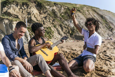 Glücklicher Mann tanzt mit seinem Freund am Strand und spielt Gitarre - PBTF00141