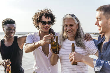 Lächelnde Freunde stoßen mit Bierflaschen am Strand an einem sonnigen Tag an - PBTF00146