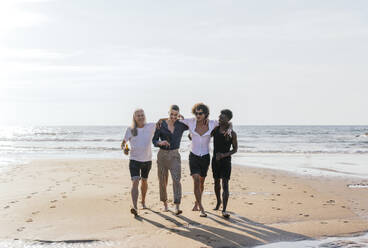 Multi-ethnic friends with arms around walking at beach - PBTF00147