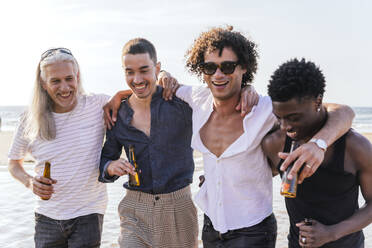 Cheerful friends with beer bottles walking at beach - PBTF00149