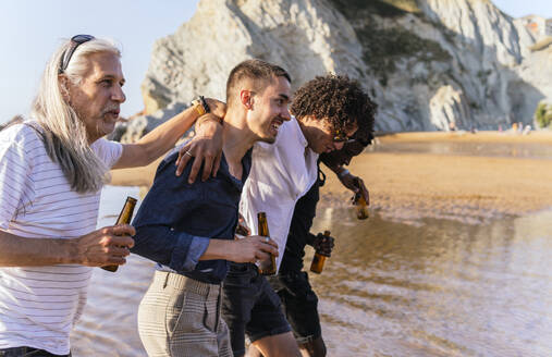 Friends having beer and strolling together at beach on sunny day - PBTF00150