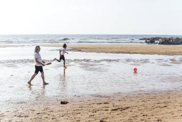 Freunde laufen hinter einer Plastikscheibe am Strand an einem sonnigen Tag - PBTF00151