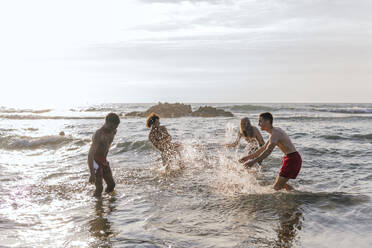 Carefree friends enjoying splashing water on each other in sea - PBTF00156