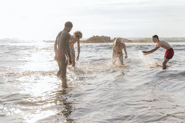 Multi-ethnic friends enjoy splashing water on each other in sea - PBTF00157