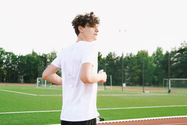 Teenage boy running in stadium under sky - YHF00071