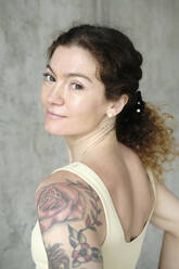 Smiling woman with tattoo in front of concrete wall - YHF00078