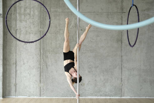Frau übt Gymnastik an einer Stange vor einer Betonwand - YHF00082