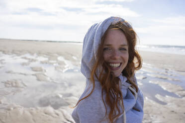 Glückliche Frau mit Kapuzenshirt am Strand im Urlaub - KNSF09716