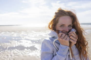 Redhead woman covering face in hooded shirt at beach - KNSF09718