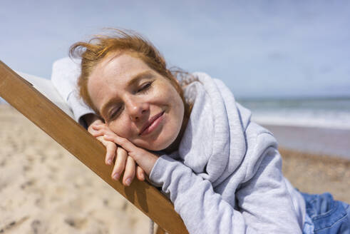 Woman relaxing on deck chair at beach - KNSF09721