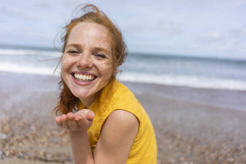 Fröhliche Frau gestikuliert am Strand im Sommerurlaub - KNSF09722