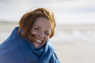 Glückliche Frau in Schal eingewickelt am Strand - KNSF09726
