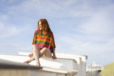 Lächelnde Frau, die auf der Spitze einer Strandhütte sitzt - KNSF09731