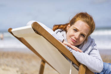 Woman relaxing on deck chair at beach - KNSF09737