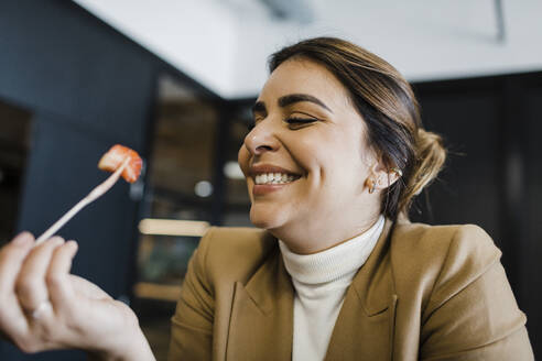 Glückliche Geschäftsfrau isst Erdbeere mit Gabel im Büro - DCRF01782