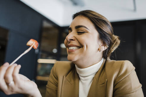 Happy businesswoman eating strawberry with fork at office - DCRF01782