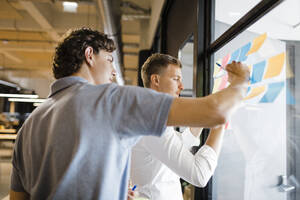 Businessmen writing on adhesive notes at office - DCRF01791