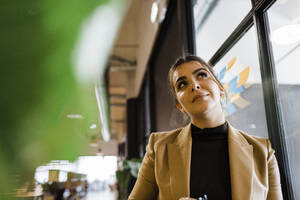 Thoughtful businesswoman leaning on wall at workplace - DCRF01798