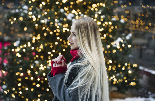 Happy blond woman standing in front of Christmas tree - YBF00116