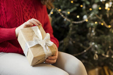 Woman holding wrapped Christmas gift at home - ONAF00626