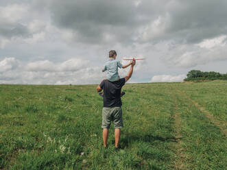 Father carrying son on shoulders and playing in meadow - VSNF01325