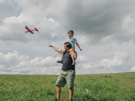 Vater und Sohn spielen zusammen mit einem Spielzeugflugzeug auf einer Wiese - VSNF01327