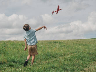Junge fliegt Spielzeugflugzeug auf einer Wiese - VSNF01328
