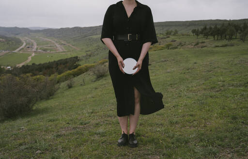 Frau in schwarzem Kleid hält Spiegel auf grüner Landschaft - YBF00122