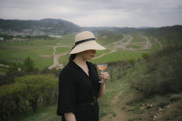 Frau mit Strohhut hält ein Glas Wein auf einer Wiese - YBF00127