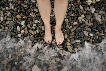 Legs of woman on pebble beach by sea - YBF00138