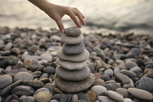 Hand of woman stacking pebbles at beach - YBF00141