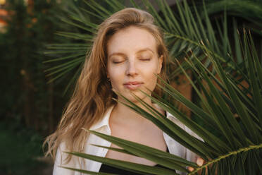 Young woman with eyes closed near green leaves - YBF00143