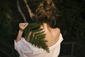 Young blond woman holding fern covering her shoulder - YBF00145