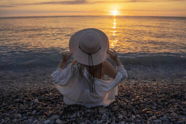 Young woman wearing hat and enjoying sunset at beach - YBF00149